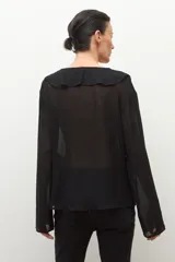 Blusa negra de manga larga, confeccionada en tela liviana y semitransparente, con escote en V adornado con volados y un botón frontal.