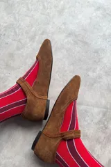 Mocasín de gamuza color marrón, con diseño plano, punta cuadrada y tira en el empeine con hebilla metálica dorada.