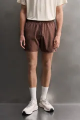 Short deportivo de entrenamiento en color marrón, confeccionado en tejido técnico ligero y elástico. Cuenta con cintura elástica ajustable con cordón, bolsillos frontales, bolsillo trasero con cierre y aberturas laterales en el bajo. Incluye un pequeño detalle de logo estampado en la pierna.