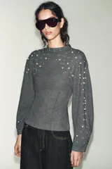 Jersey de cuello perkins y manga larga en color gris oscuro, con detalle de aplicaciones de perlas distribuidas en la parte superior y a lo largo de las mangas.