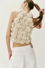 Top corto de cuello halter, confeccionado con una estructura de tejido que forma flores en relieve por toda la prenda. Presenta cierre en la espalda con abertura y botón oculto.
