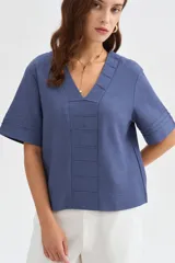 Blusa de viscosa color beige con cuello en V, mangas cortas amplias y detalles de pespuntes decorativos en el frente y las mangas.