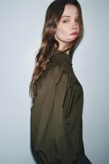 Camisa de popelín color blanco con cuello solapa, cierre frontal con botones ocultos y mangas largas abullonadas con puños estructurados.