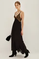 Vestido largo de fiesta con escote en V profundo y tirantes finos. Presenta un cuerpo superior bordado con lentejuelas doradas y una falda fluida de color negro con caída suave.