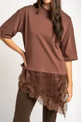 Remera oversize marrón con corte a la altura de la cadera, cuello redondo y mangas cortas holgadas. Incorpora un aplique inferior superpuesto de satén con detalles de encaje bordado en los bordes.