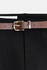 Pantalón tobillero de tiro medio, color beige, con pinzas delanteras y bolsillos frontales. Incluye un cinturón fino de cuero marrón con hebilla metálica dorada y cierre frontal con cremallera, botón interior y gancho.