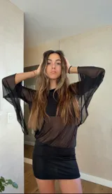 Vestido corto negro de diseño asimétrico con un hombro al descubierto. Presenta mangas largas acampanadas de tela semitransparente y una falda ajustada al cuerpo.