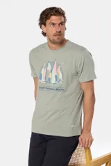 Remera de manga corta color verde grisáceo con cuello redondo. Presenta un estampado frontal de veleros sobre un fondo circular con líneas verticales, y texto bordado debajo.
