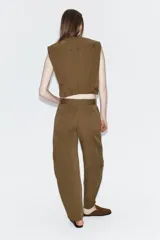 Pantalón cargo de tiro alto en color marrón tostado, con diseño de pernera holgada que se estrecha hacia el tobillo. Presenta bolsillos frontales con cierre de cremallera, bolsillos laterales de plastrón con solapa y botón, y cierre frontal con cremallera y botón.