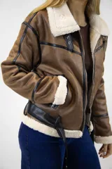 Campera estilo aviador de cuero sintético marrón con interior y detalles de corderito sintético en color crudo. Cuenta con cierre frontal metálico, detalles de tiras con hebilla en el cuello y el ruedo, y ribetes en color negro.