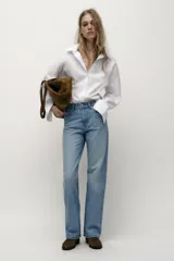 Jeans de tiro alto con diseño de cinco bolsillos, pernera recta y corte largo. Presenta cierre frontal con cremallera y botón metálico.