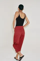 Jeans capri de tiro medio y pernera balloon, color rojo ladrillo. Confeccionados en denim, cuentan con trabillas en la cintura, bolsillos delanteros y traseros, y cierre frontal con cremallera y botón metálico.