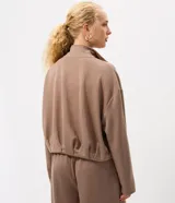 Campera de modal color marrón, con cuello alto, cierre frontal completo y diseño con pliegues en el ruedo. Presenta mangas largas y un calce holgado.