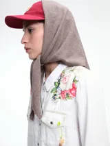 Triángulo tipo capucha con lazo, confeccionado en tejido de punto suave. Presenta un diseño versátil que puede usarse como pañuelo o accesorio para la cabeza.