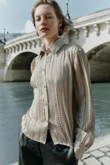 Camisa de manga larga con cuello solapa, confeccionada en tejido satinado con textura efecto arrugado y cierre frontal con botones dorados.