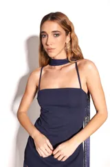 Vestido largo de color azul marino con base de crepé asimétrica y sobrecapa de microtul translúcido. Presenta un diseño de escote recto sin breteles y falda con transparencia. Incluye un accesorio de tela a juego versátil para usar como chal o lazo al cuello.