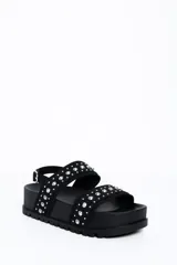 Sandalia chunky de plataforma color negro, con diseño de doble tira ancha decorada con tachas metálicas cónicas y pulsera ajustable al tobillo con hebilla.