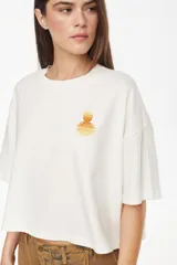 Remera boxy de algodón con elastano, color blanco crudo, de manga corta y calce relajado. Cuenta con un delicado bordado de un atardecer en el pecho.