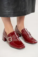 Mocasin de cuero charolado color bordó, con punta cuadrada, taco bloque bajo y detalle de tira con hebilla metálica plateada en el empeine.