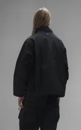 Campera técnica liviana de microfibra negra con acabado mate, capucha ajustable, cierre frontal oculto bajo solapa, bolsillos frontales con solapa y cordón ajustable en la cintura.