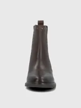 Bota tipo botín de cuero color marrón oscuro, con elásticos laterales y detalles de tachas metálicas doradas a lo largo de la caña. Cuenta con suela gruesa y taco cuadrado de altura media.