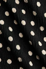 Vestido midi en punto texturizado de color negro con estampado de lunares blancos, escote redondo y manga corta. Cuenta con cintura entallada.