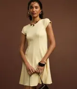 Vestido corto color amarillo pálido, con escote redondo y mangas cortas. Presenta recortes verticales en el torso que definen la silueta y una falda ligeramente acampanada.