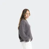 Buzo tejido de punto ochos en color gris, con cuello redondo, mangas largas y detalles de efecto roto en puños y ruedo. Presenta un pequeño logo bordado en el centro del pecho.