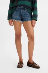 Short de denim de tiro bajo para mujer, confeccionado en algodón con baja elasticidad. Presenta un lavado azul medio con efecto desgastado, diseño de cinco bolsillos y dobladillo deshilachado con flecos.