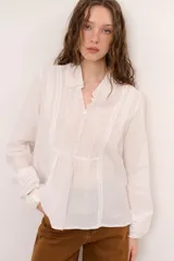 Camisa blanca de manga larga con detalles bordados en el frente, cuello redondo con solapas delicadas, cierre frontal con botones y puños anchos con encaje.