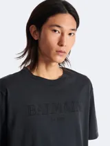 Remera gris oscuro de algodón con cuello redondo y mangas cortas. Estampado frontal con el logo de Balmain en relieve.