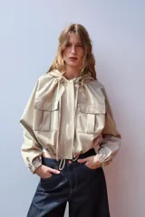 Cazadora color beige con capucha ajustable, manga larga con puño elástico, bolsillos frontales con solapa, bajo ajustable y cierre frontal con cremallera y botones a presión.