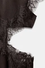 Vestido midi negro de tejido satinado con cuello redondo y manga capa. Presenta detalles de cut-out laterales adornados con encaje a tono. El bajo es asimétrico y tiene cierre en la espalda.