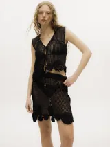 Top de crochet color marrón con tejido calado, diseño sin mangas y cierre frontal con cuerdas y cuentas de madera. Presenta apliques tejidos en el ruedo.