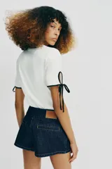 Camiseta de algodón de corte regular, color blanco con detalles de vivos y lazos en contraste negro en el cuello y en las mangas cortas.