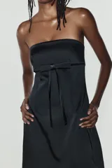 Vestido mini satinado negro con escote palabra de honor y detalle de lazo en el frente.