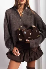 Cartera tipo baguette de gamuza color chocolate, con diseño decorado con diversos apliques metálicos, perlas y piezas de piedra. Cuenta con cierre superior y correa ajustable.