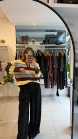 Sweater tejido de punto con diseño a rayas horizontales en tonos amarillo, celeste y marrón. Presenta un cuello polo con escote en V, mangas largas y un corte holgado.