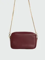 Cartera crossbody de cuero negro con diseño rectangular, cierre superior y correa de cadena dorada. Presenta el detalle de una estrella característica de la marca grabada en el frente.