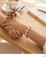 Pulsera elástica compuesta por una alternancia de perlas blancas y esferas metálicas plateadas.