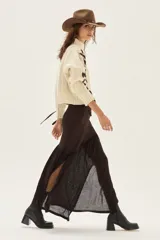 Falda larga de punto en color marrón, confeccionada en una mezcla de viscosa y lurex. Presenta un diseño de corte asimétrico con un volado en el bajo que aporta movimiento y ligereza a la prenda.