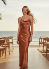 Vestido largo tipo slip dress de satén color cobre, con escote drapeado (cowl neck) y breteles finos. Presenta un corte al bies que se ajusta suavemente a la silueta con caída fluida.