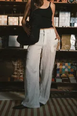 Pantalón de corte recto y tiro alto, confeccionado en lino color blanco. Presenta cierre frontal con botón y bolsillos laterales.