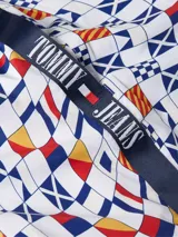 Short de baño blanco con estampado de banderas náuticas en azul, rojo y amarillo. Tiene cintura elástica con cordón ajustable, bolsillos laterales y logo de Tommy Jeans en la pierna.