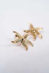 Aros tipo stud con diseño de estrella de mar en acabado plateado con textura rugosa.