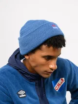 Gorro tipo beanie de tejido de punto color blanco crema, con parche frontal que incluye el logo de Umbro y la inscripción Nacional.