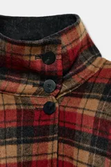 Capa oversize de corte amplio con estampado de cuadros en tonos rojos, negros y marrones. Presenta cuello alto, cierre frontal con botones, bolsillos delanteros y mangas ajustables mediante trabillas con botones.