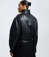 Campera estilo bomber de cuero sintético (PU) color negro, con cuello alto estructurado, cierre frontal con cremallera y botones a presión, mangas largas y detalle de cinturón ajustable en la cintura.