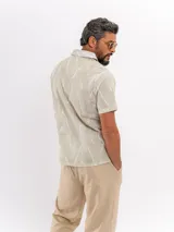 Camisa de manga corta de algodón en color beige, con cuello camisero y cierre frontal de botones, con diseño estampado sutil.