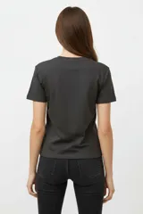 Remera de algodón negra de manga corta y cuello redondo, con estampa frontal que incluye letras rojas y gráficos en tonos dorados.